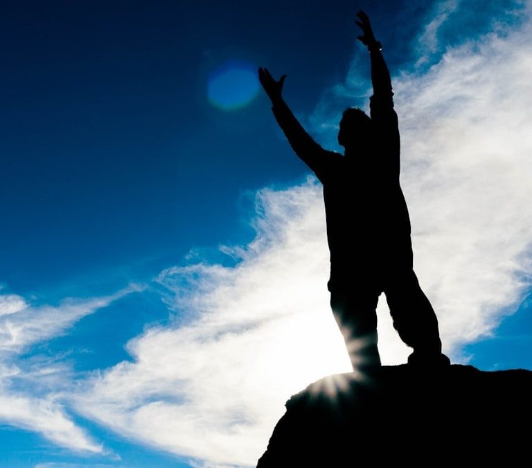 silhouette of man raising his hands under blue sky during daytime